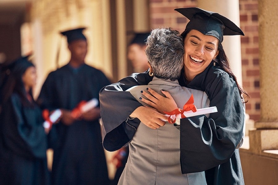 young female graduate in a cap and gown hugging her father in celebration